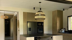 Een moderne keuken met een centraal eiland, barkrukken, een hanglamp en houten keukenkastjes.