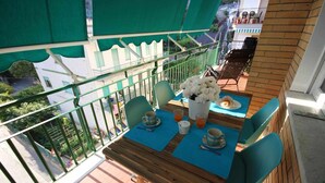Un balcón con una mesa de madera dispuesta para dos personas, un jarrón con flores blancas y vistas a la calle.