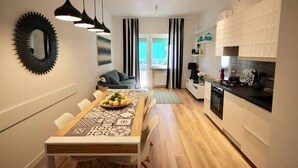 Una cocina moderna con zona de comedor, que presenta una mesa de madera con mantel estampado, cortina a rayas negras y blancas y luces colgantes.