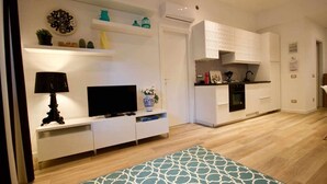 Una sala de estar moderna con una televisión de pantalla plana, una lámpara y un jarrón decorativo sobre un mueble blanco.
