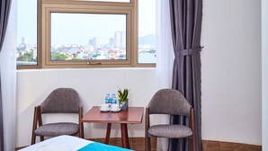 A hotel room with a bed, two chairs, a small table with a plant and water bottles, and a view of a cityscape through a large window. - BOBO Boutique Hotel (Ho Chi Minh City)