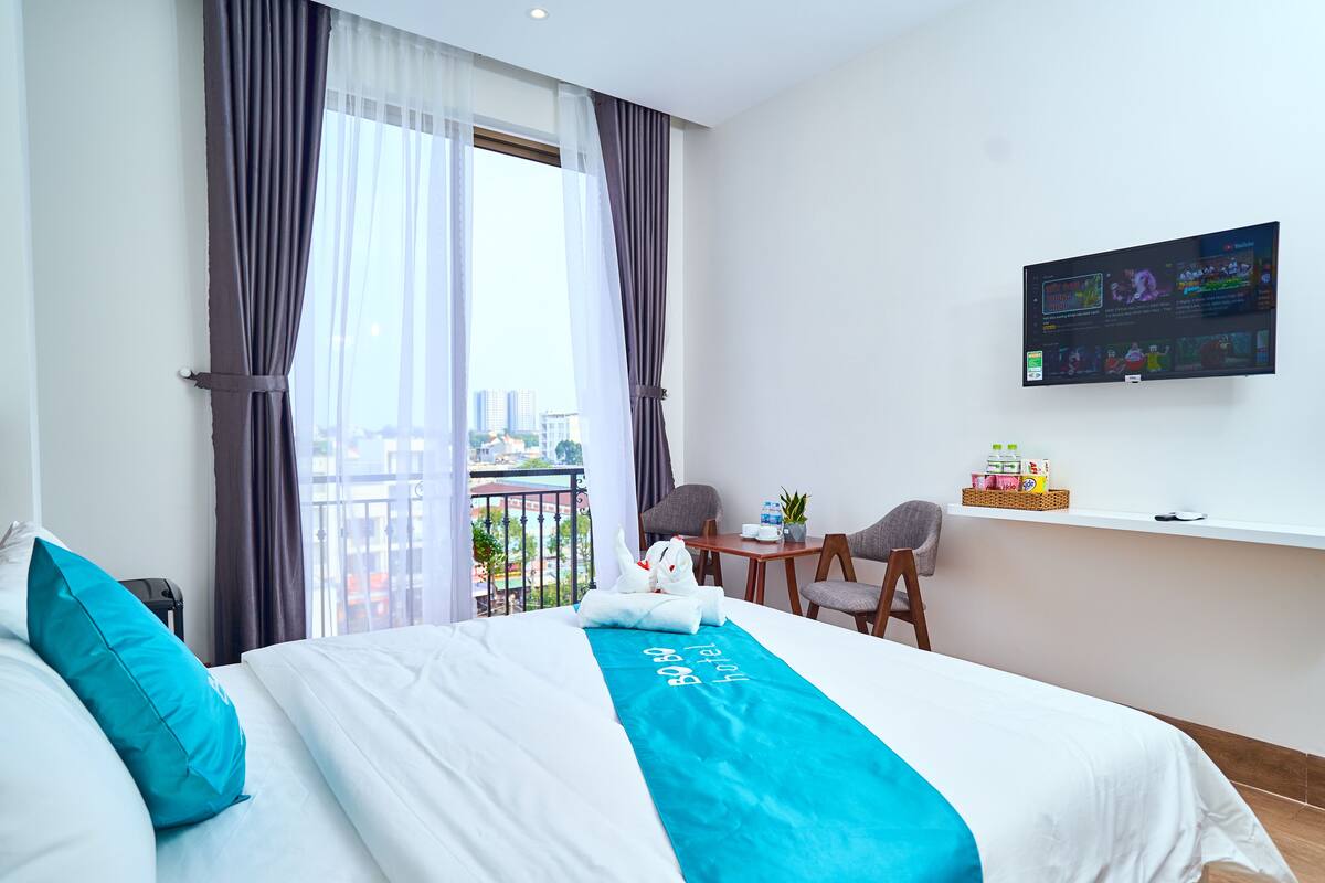 Ein Hotelzimmer mit Bett, einem an der Wand befestigten Fernseher, einem Balkon mit Blick und einem kleinen Tisch mit Stühlen.
