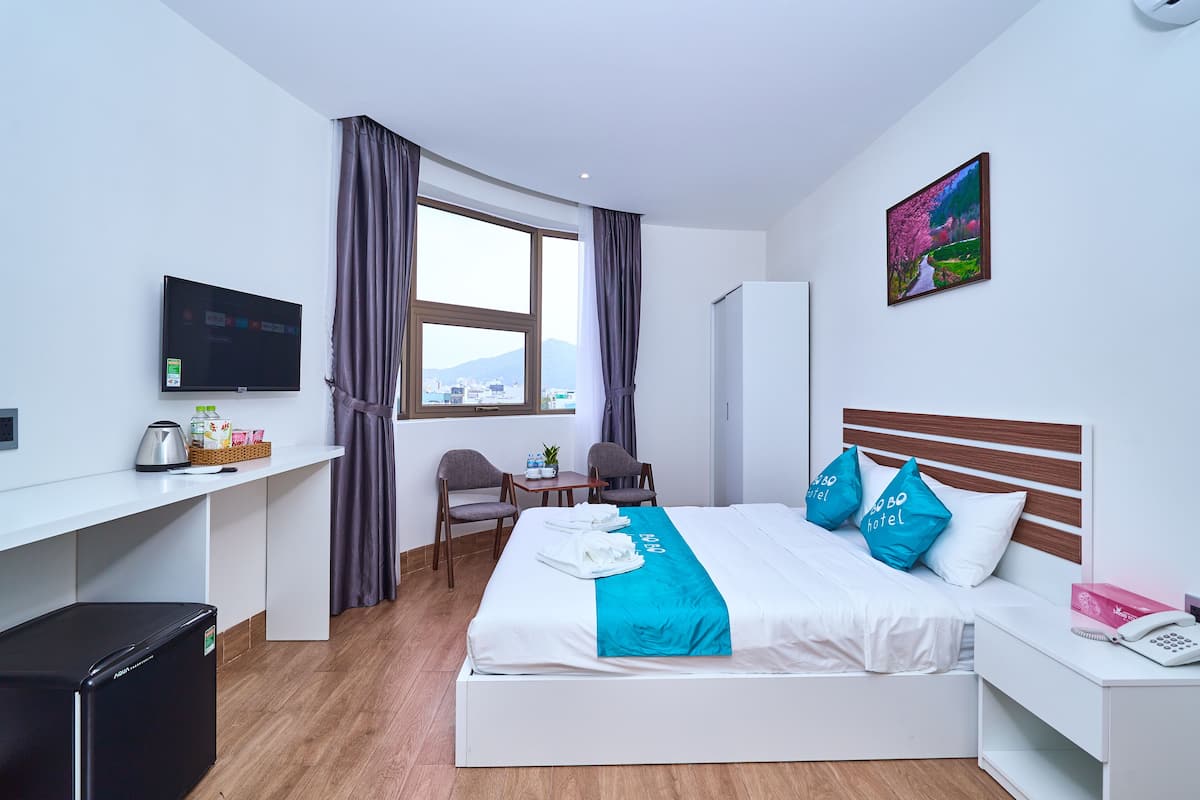 Ein Hotelzimmer mit Bett, Schreibtisch, Fernseher, Kühlschrank und einem Fenster mit Vorhängen.