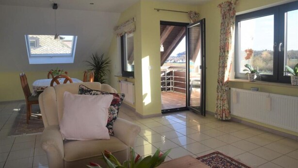 Ein geräumiges Wohnzimmer mit Sofa, Esstisch und Blick ins Freie.