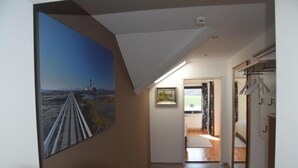 Ein Flur mit einem großen Gemälde einer Brücke, einem Holzboden und Blick in ein Schlafzimmer mit Bett und Kommode.