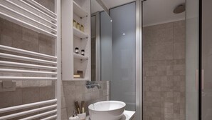 Une salle de bain moderne avec un grand miroir, un lavabo blanc et une cabine de douche en verre.