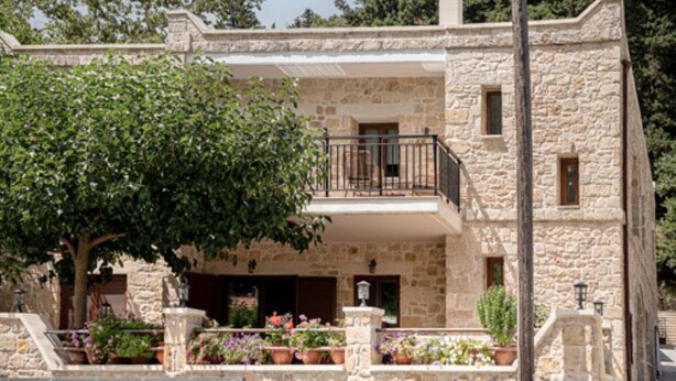 Un bâtiment en pierre doté d’un balcon, de plantes en pot et d’un arbre devant.