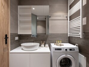 Une salle de bain moderne avec un grand lavabo, un miroir, un lave-linge encastré et un porte-serviettes.