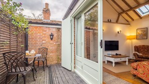 A cozy room with a brick wall, a white door, a television, a patterned sofa, and a table with a teapot. - The Stables, Edingthorpe, Norfolk (North Walsham)