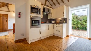 A modern kitchen with white cabinets, stainless steel appliances, and a wooden floor. - The Stables, Edingthorpe, Norfolk (North Walsham)
