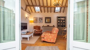 A cozy living room with a sofa, armchairs, a coffee table, and a TV. There are framed pictures on the wall, a bookshelf, and a radiator. - The Stables, Edingthorpe, Norfolk (North Walsham)