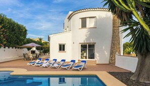 Un bâtiment blanc avec une piscine, des chaises longues bleues et un palmier.