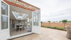 A modern house with a large open-plan living area, a dining room, and a patio with stone flooring. - Field Piece Cottage, Burnham Market, Norfolk (Burnham Market)
