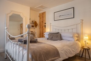 Une chambre à coucher avec un lit à baldaquin blanc, une porte en bois, un tableau encadré au mur et une table de chevet avec une lampe.