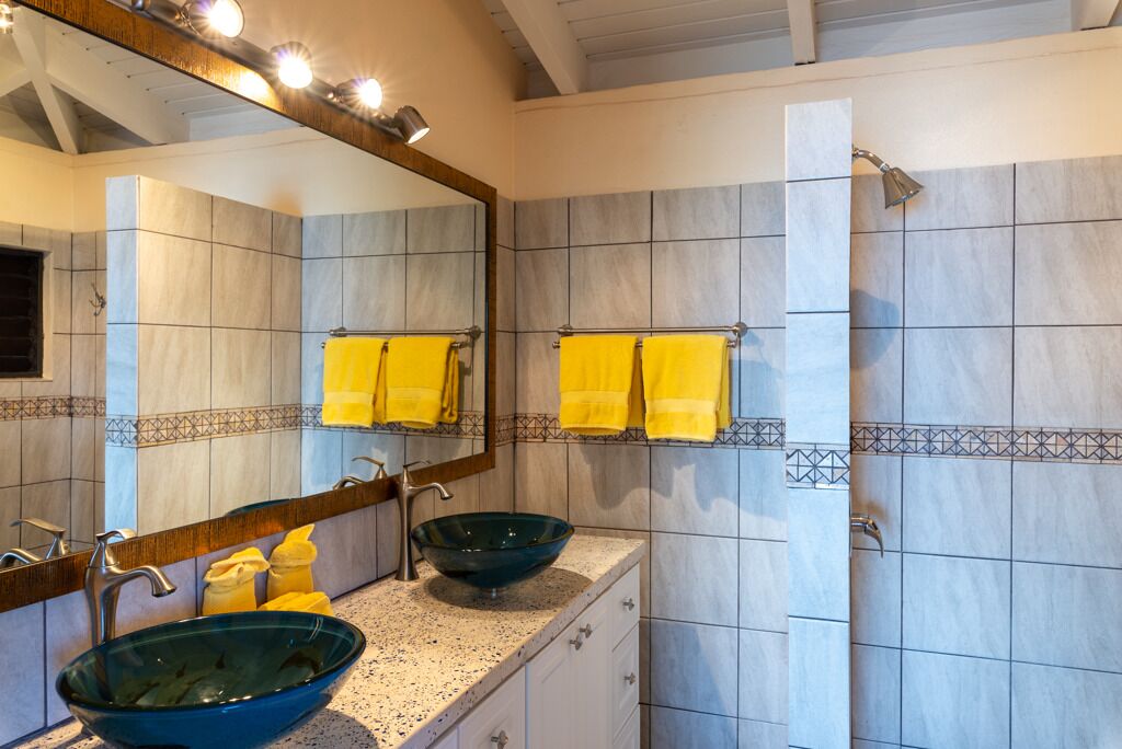 A bathroom with a large mirror, two sinks, yellow towels, and a shower area.