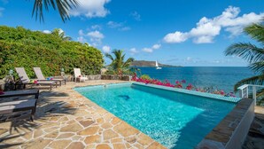 Une piscine d’un bleu éclatant, dotée de chaises longues, entourée d’une végétation luxuriante et offrant une vue sur la mer.