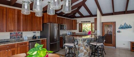 A spacious kitchen with wooden cabinets, a stainless steel refrigerator, and a stone island with bar stools.