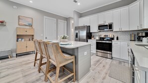 A modern kitchen with white cabinets, stainless steel appliances, and a central island with seating. - North Hampton: Luxury Gulf Shores Escape (Gulf Shores)