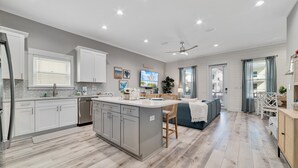 A modern kitchen with a central island, white cabinetry, and a dining area with a sofa and chairs. - North Hampton: Luxury Gulf Shores Escape (Gulf Shores)
