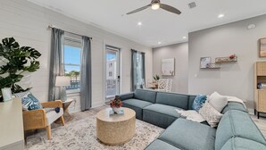 A modern living room with a grey sectional sofa, a round wicker coffee table, and a large potted plant. - North Hampton: Luxury Gulf Shores Escape (Gulf Shores)