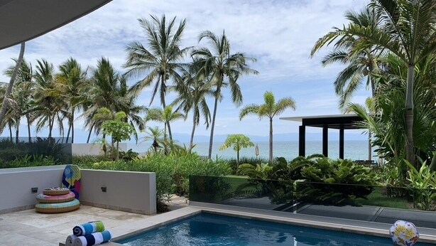 Una piscina con vistas al océano, rodeada de palmeras y una zona techada.