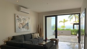Una sala de estar moderna con un sofá modular, una mesa de centro y un ventanal con vistas al océano y palmeras.
