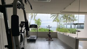 Un gimnasio con equipo de ejercicio, una caminadora y vistas a palmeras y al océano.