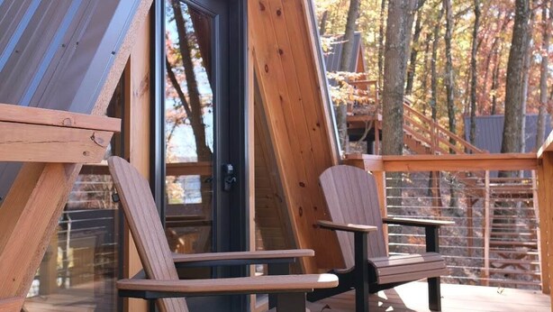 Une cabane avec un toit en pente, une terrasse en bois et deux chaises.