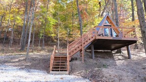 Une cabane en bois avec un escalier menant à une terrasse, entourée d’arbres aux couleurs automnales.