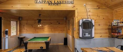 A billiards table in a room with a wooden ceiling and walls, a mounted television, and a sign reading 'TAPPAN LAKESIDE RESORT'.