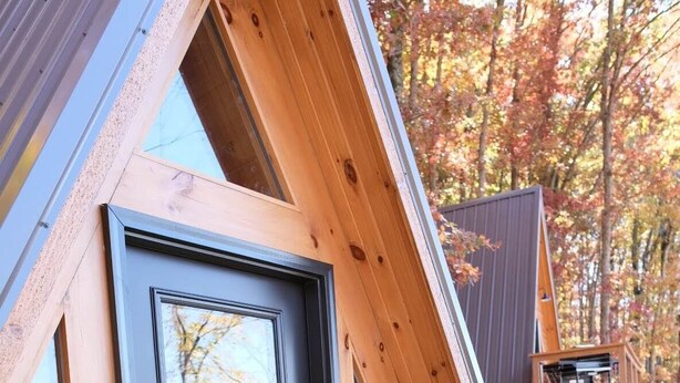 Una estructura moderna de madera triangular con puerta de cristal y zona de estar.