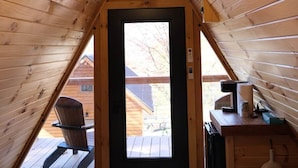 Un dormitorio acogedor en el ático con techo inclinado, una cama con colcha estampada, un escritorio con lámpara y vistas al porche exterior.