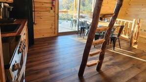 Interior de una cabaña de madera con cocina, comedor y un ventanal que da a una terraza.