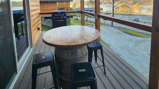 A wooden deck with a round table and two stools, overlooking a scenic landscape with a lake and autumn trees. - Yellowstone/Hot Tub-Pet friendly-Lakeview -8 Person Lodge (Scio)