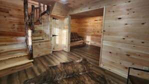 L’intérieur d’un chalet en bois, avec un escalier en colimaçon, un tapis en fourrure et un canapé.