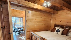 Une chambre aménagée dans une cabane en bois, avec un lit, une tête de lit en bois, un tapis tissé et un coin repas comprenant une table et des chaises.