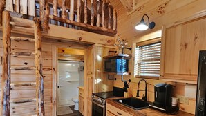 Une cuisine rustique avec des meubles en bois, une cuisinière en acier inoxydable, un évier et un escalier menant à une mezzanine.
