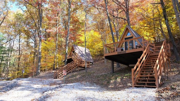 Een houten chalet met een trap naar een terras, omringd door bomen met herfstkleuren.