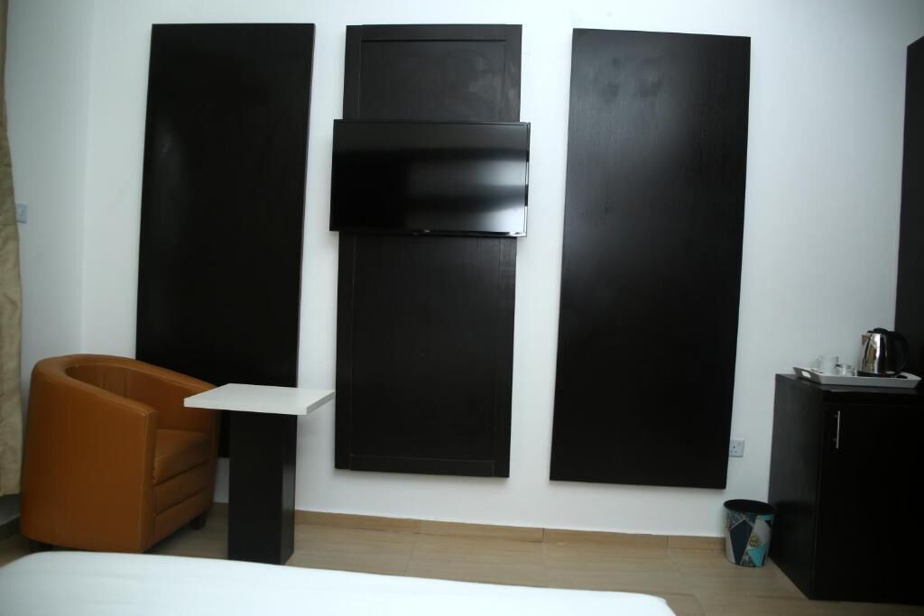 Ein Hotelzimmer mit einem Bett, einem braunen Sessel, einem kleinen Tisch, einer schwarzen Kommode und einem an der Wand montierten Fernseher.