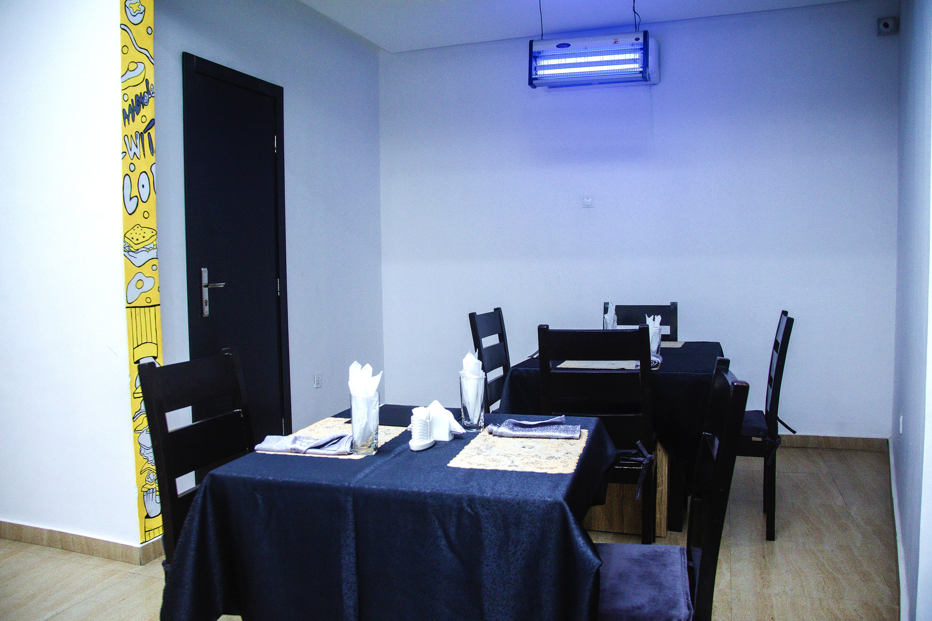 Un comedor con una mesa dispuesta para cuatro personas, sillas, una puerta negra y una pared con un diseño amarillo.