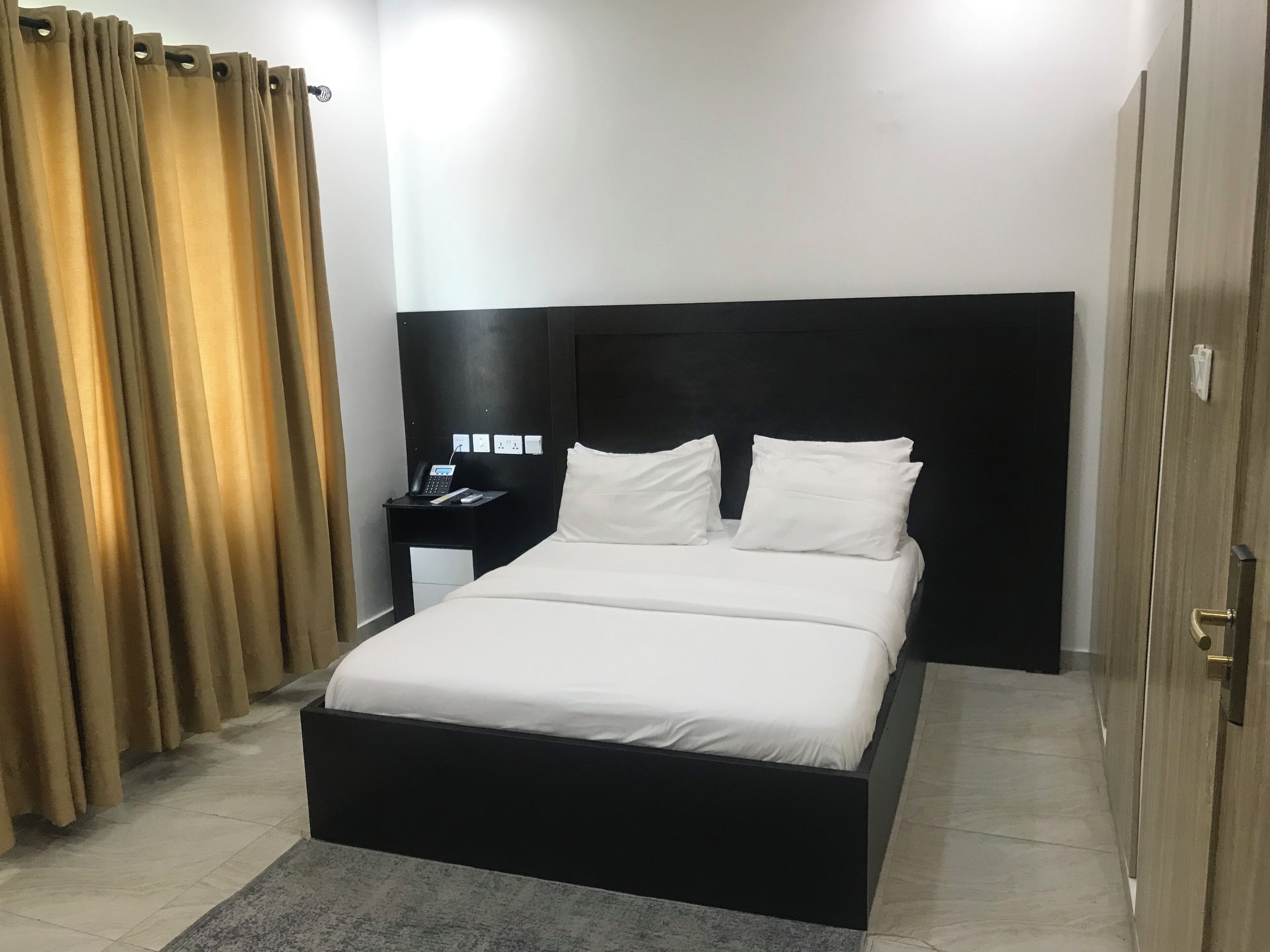 A hotel room with a large bed, a nightstand with a phone, and a curtain.