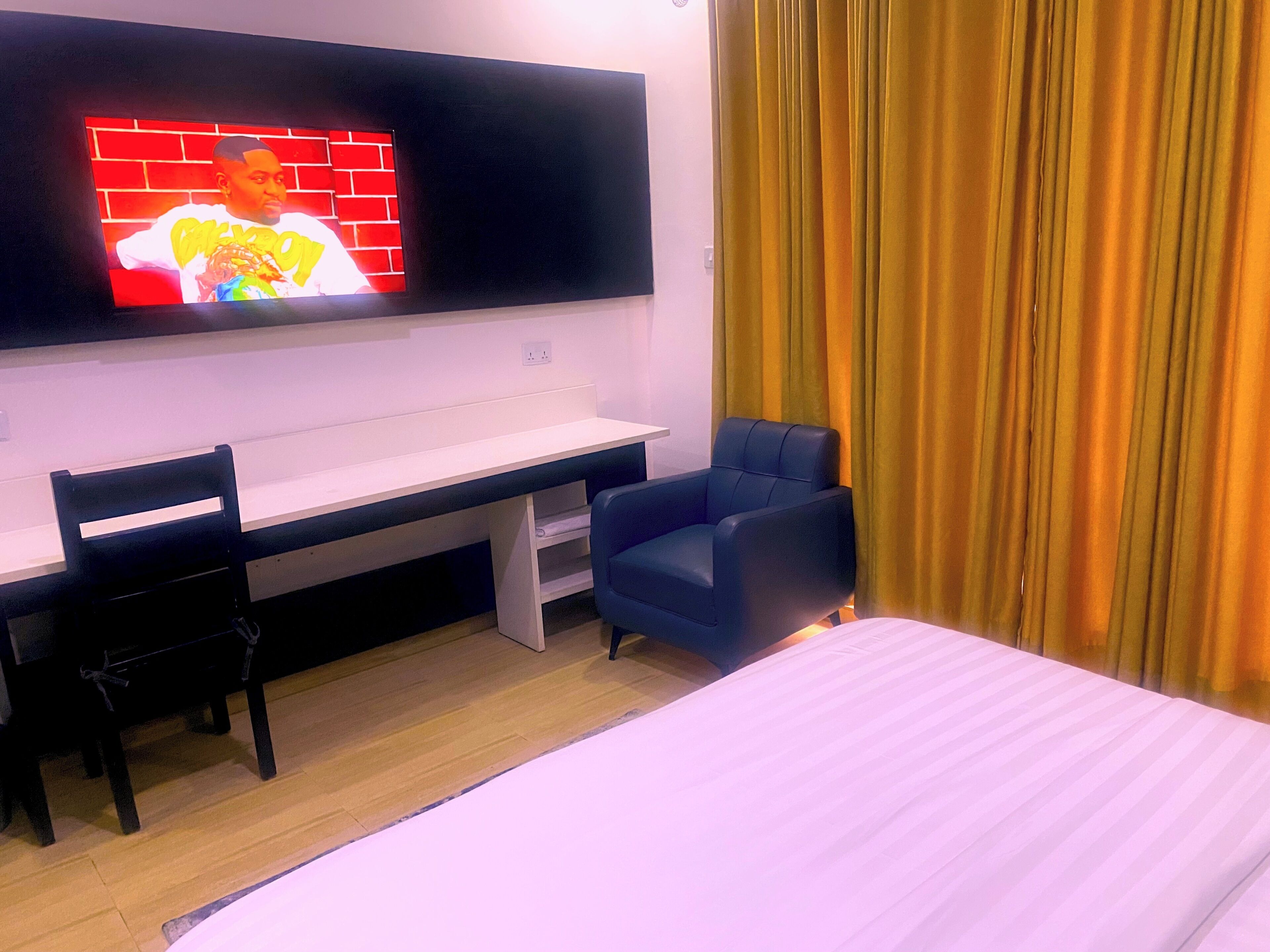 Une chambre d’hôtel avec un lit, un bureau et une chaise, un téléviseur fixé au mur et un rideau.