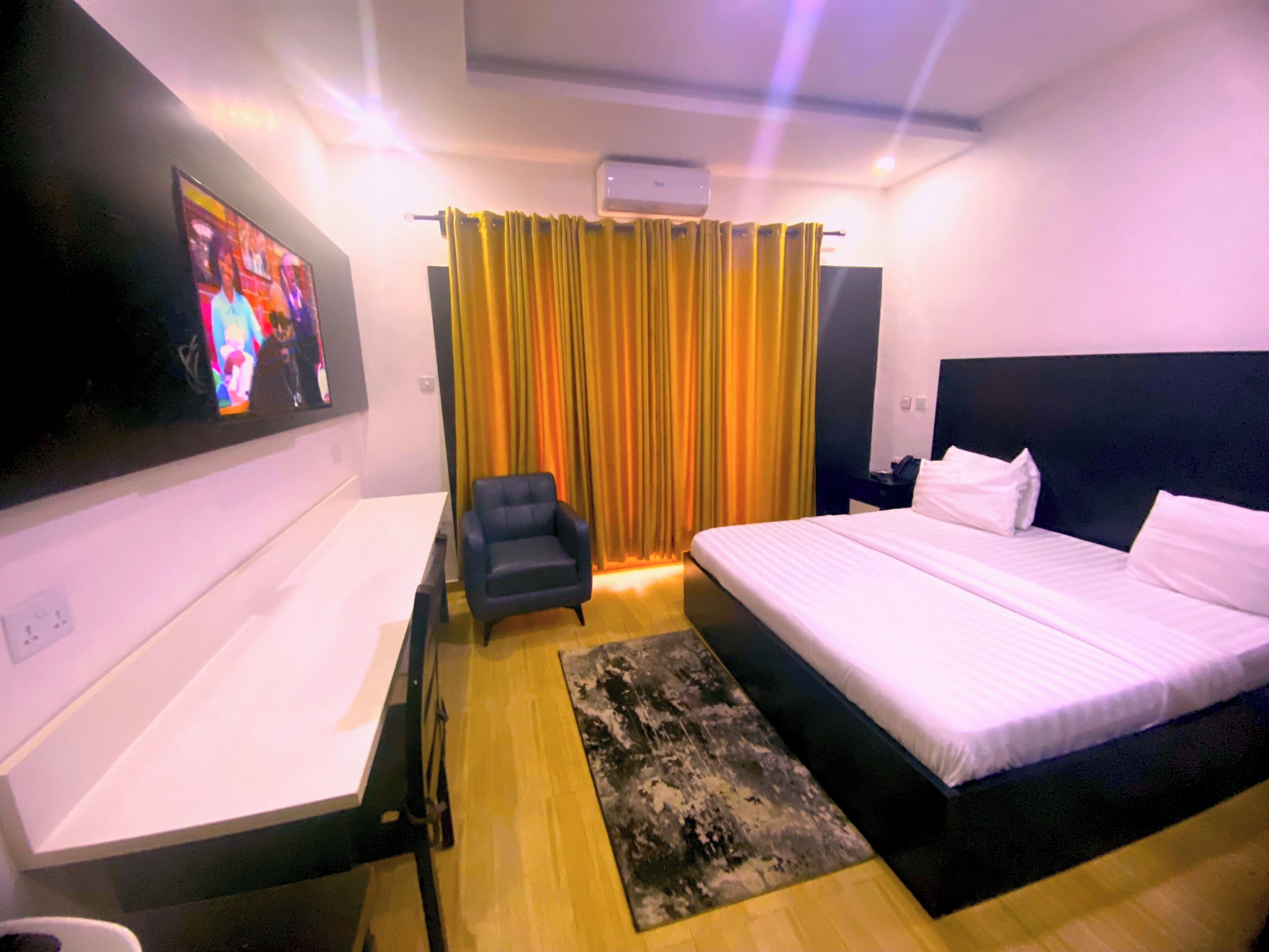 A hotel room with a bed, a desk, a chair, a TV, and curtains.