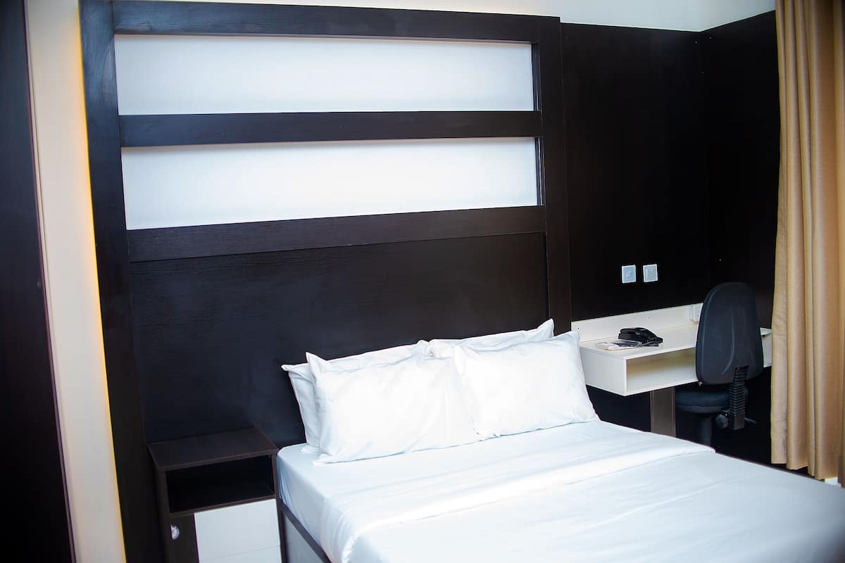 Ett hotellrum med en säng, ett skrivbord, en stol och en telefon.