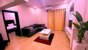 A modern living room with a sofa, a coffee table, a TV, and a potted plant. - Hotel Capitol (Lagos)