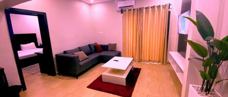 A modern living room with a sofa, a coffee table, a TV, and a potted plant.