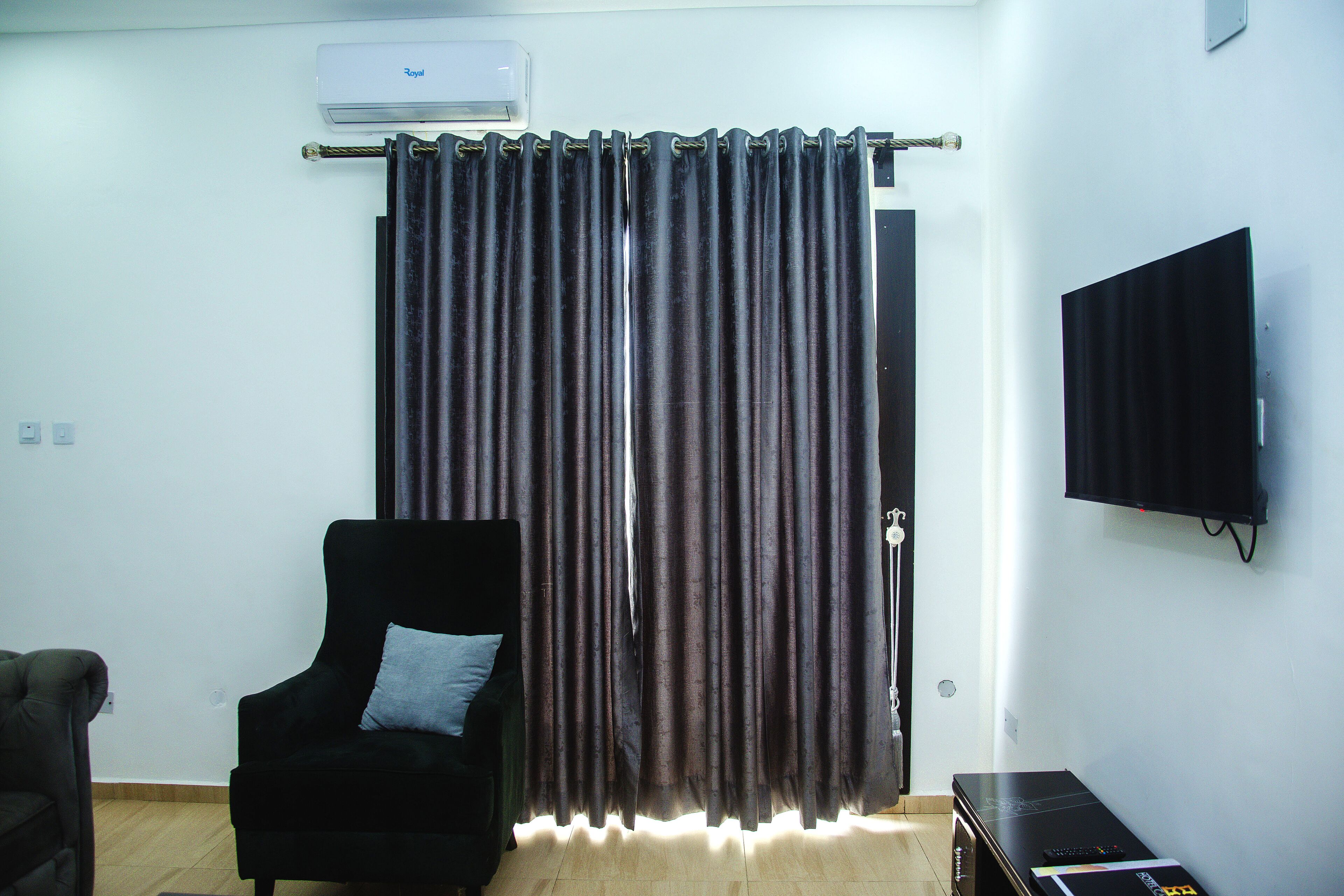 Ein Zimmer mit einem schwarzen Sessel, einem an der Wand befestigten Flachbildfernseher und einem Vorhang mit einer Metallstange.
