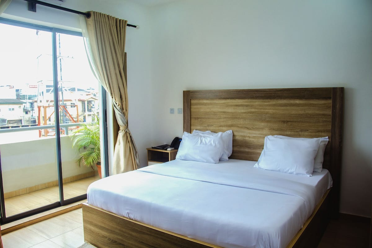 Ett hotellrum med en stor säng, ett nattduksbord, en krukväxt och utsikt över omgivningarna.
