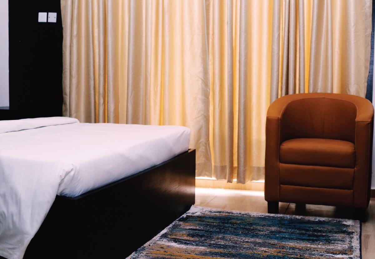 A hotel room with a bed, a chair, and a large window with curtains.