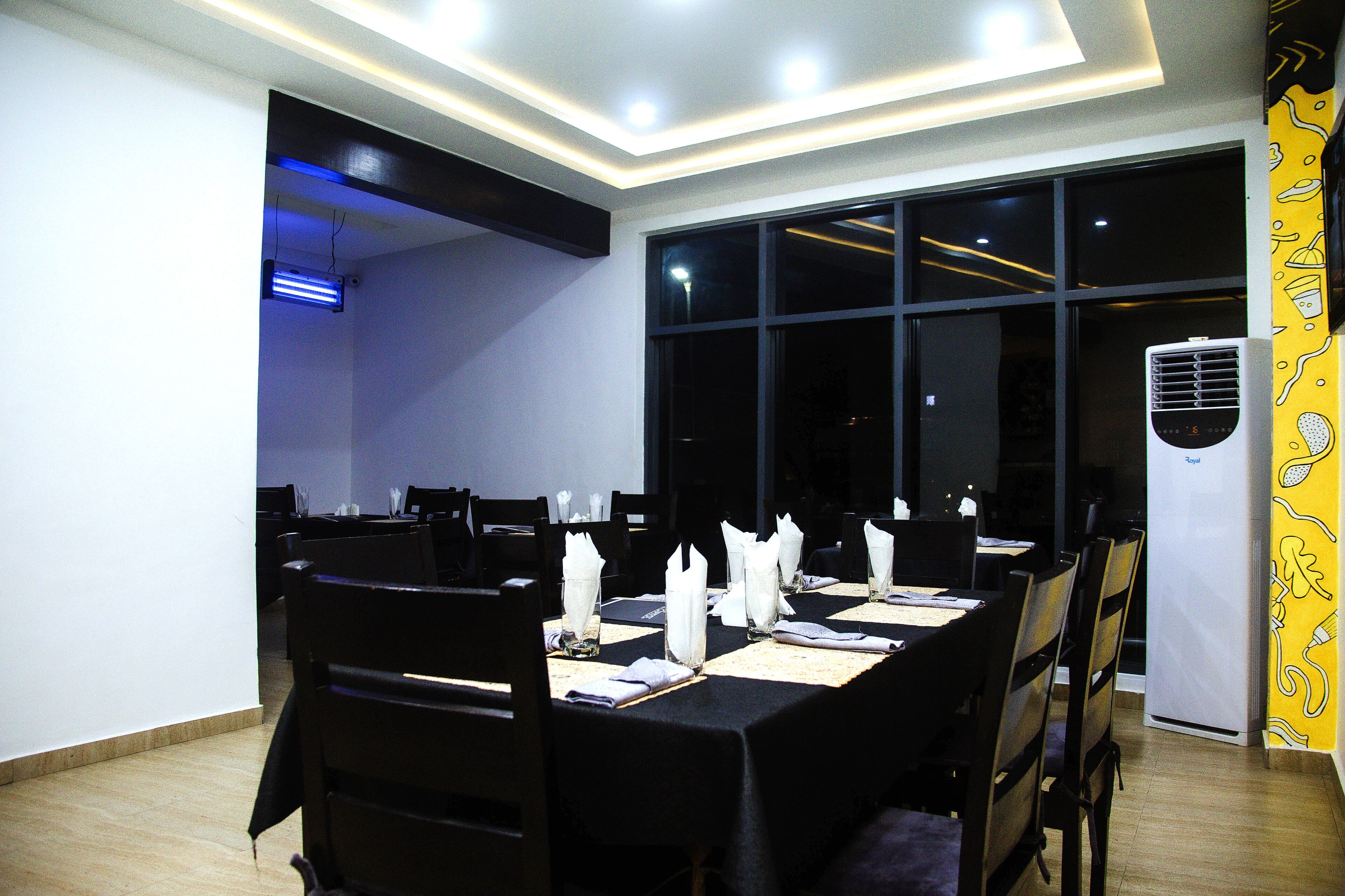 A dining area with a long table set for a meal, chairs around it, and a large window with a view of the night sky.